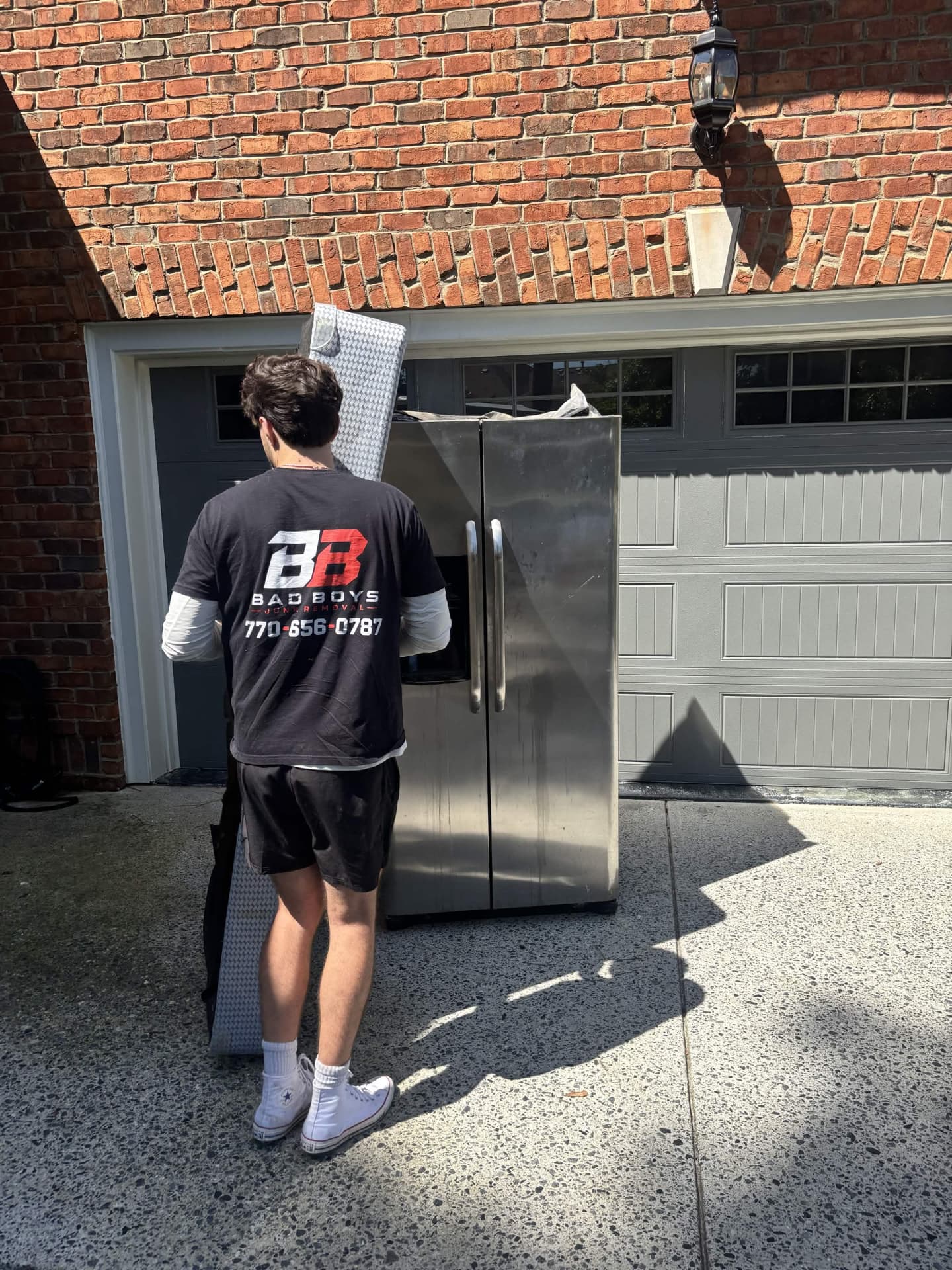 Bad Boys Junk Removal team member next to a stainless steel refrigerator and box spring in a driveway