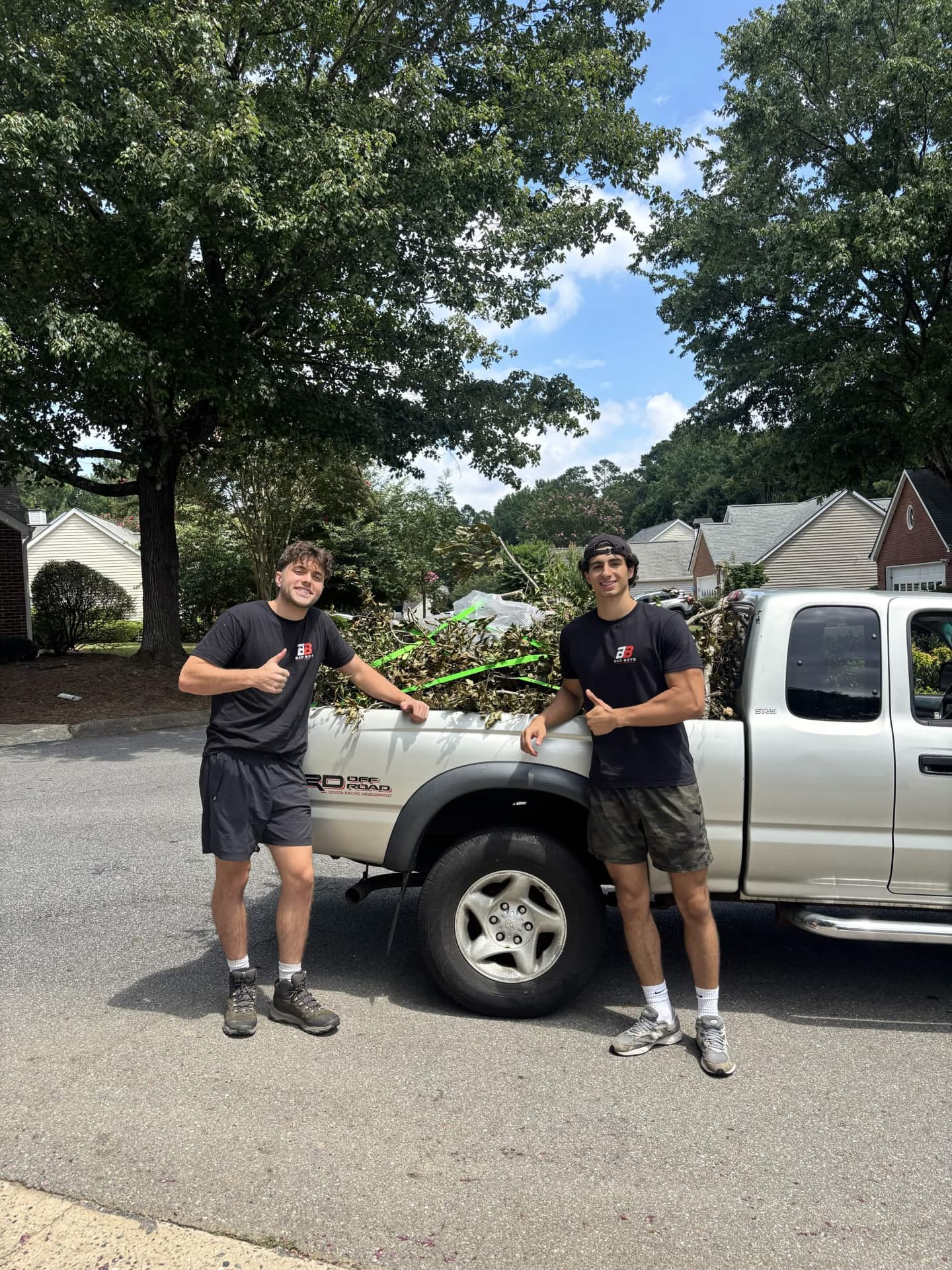 Ali and Trey giving a thumbs up beside their truck loaded with tree limbs and yard debris after a Johns Creek cleanup