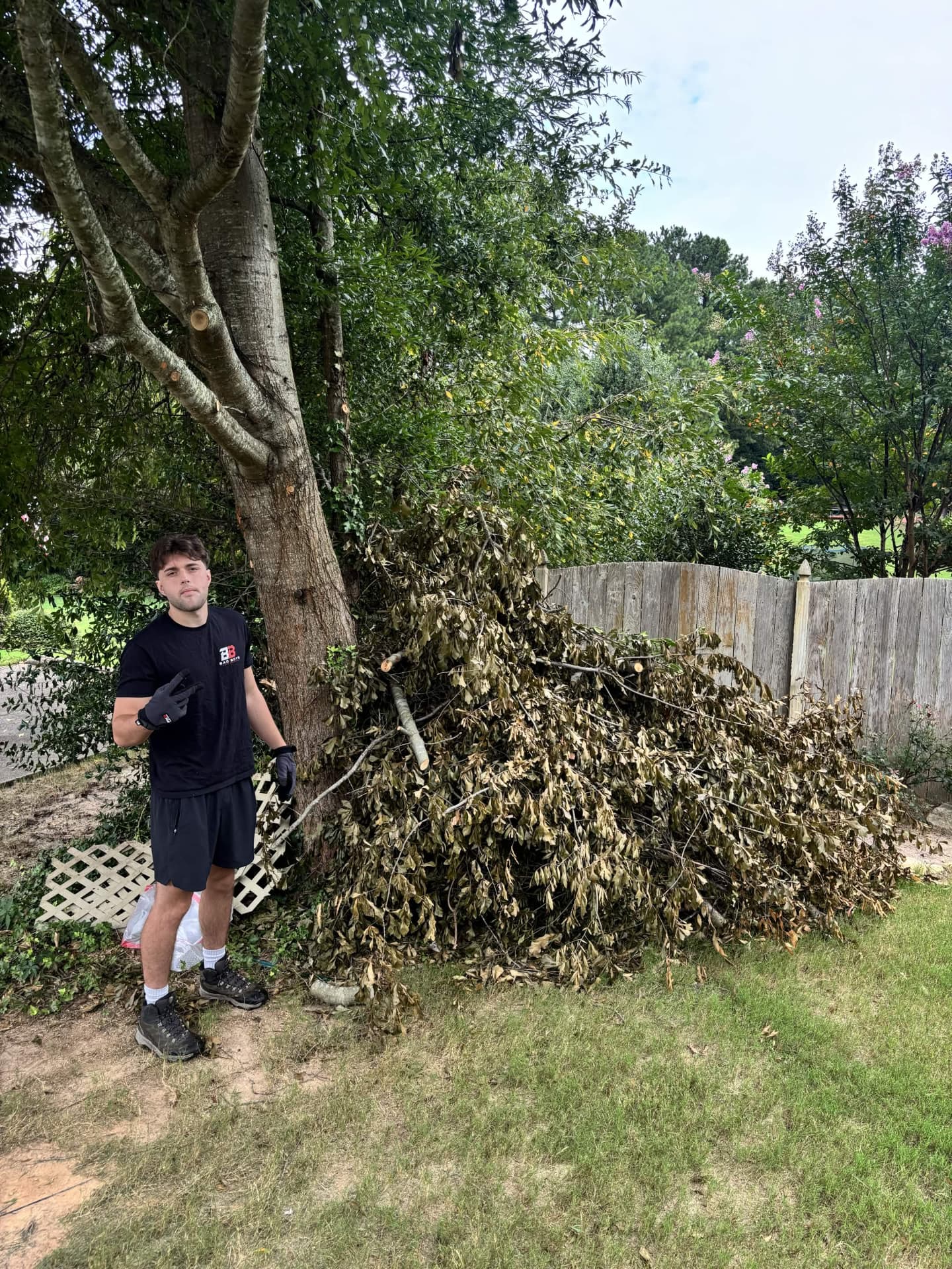 Bad Boys Junk Removal worker in gloves next to a large pile of cut tree branches in a North Atlanta backyard