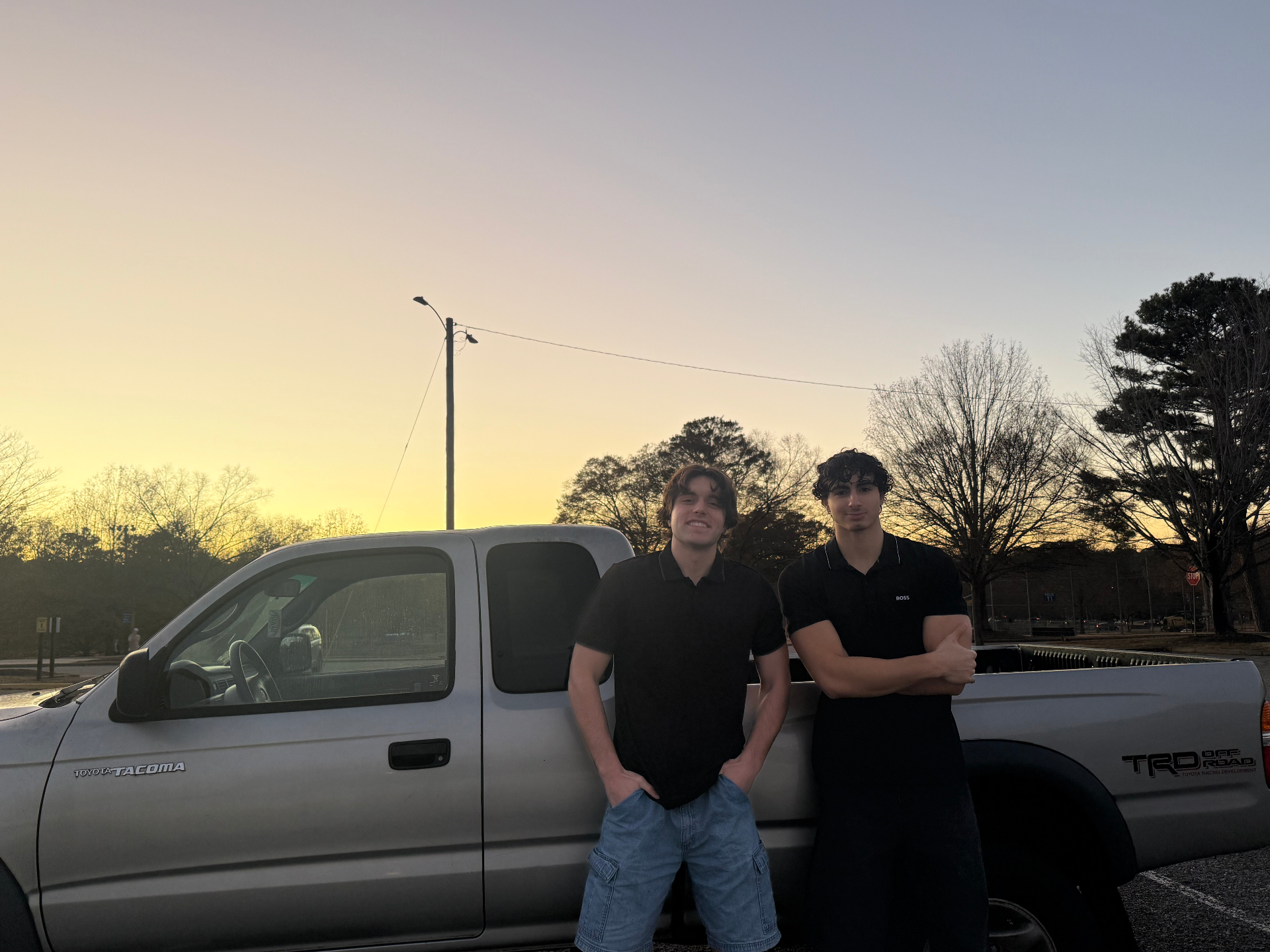 Ali and Trey, founders of Bad Boys Junk Removal, standing together by their Toyota Tacoma truck at sunset