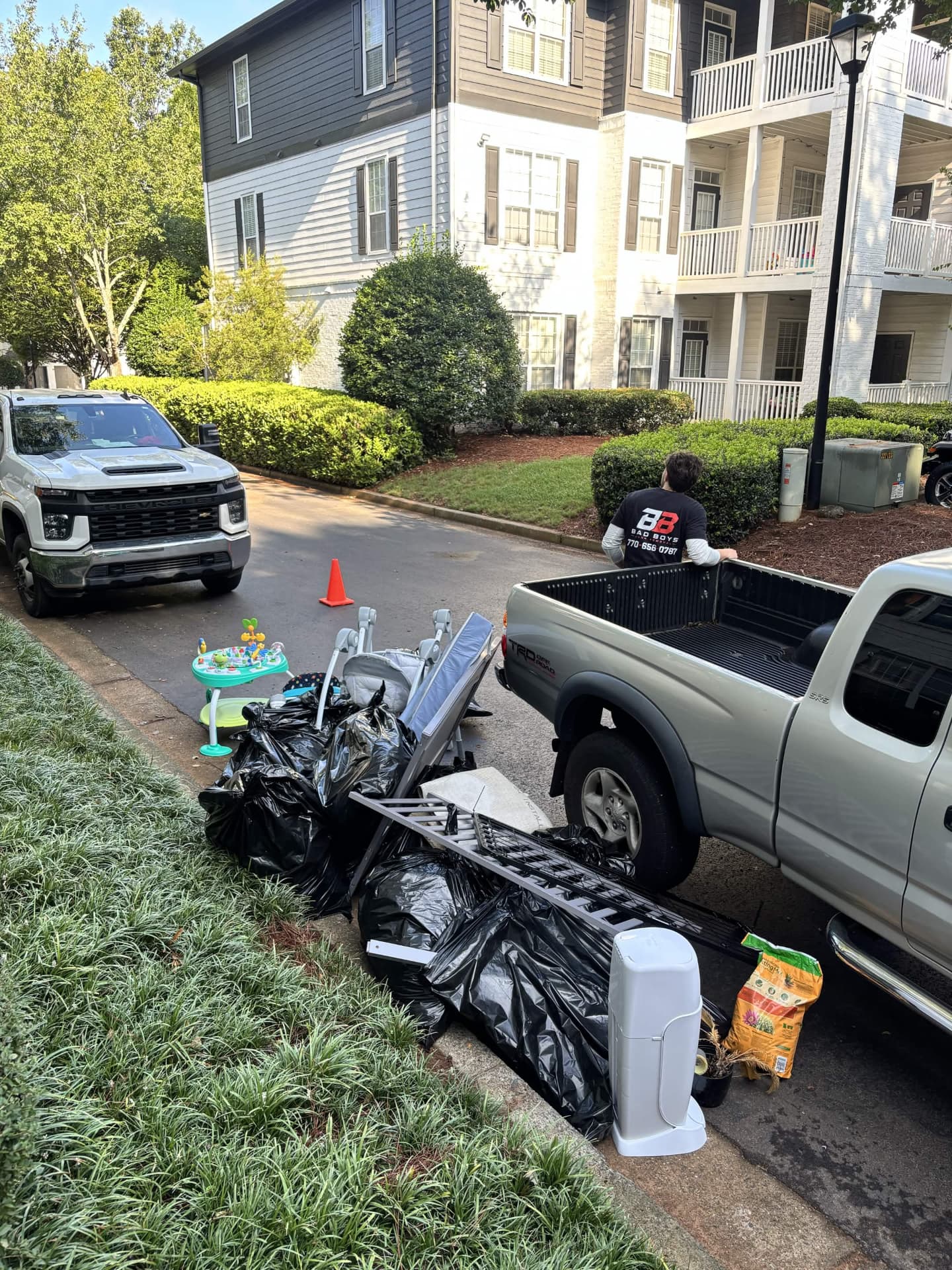 Curbside pile of bagged trash, strollers, a shelf and household junk being loaded into the truck during a Roswell cleanout