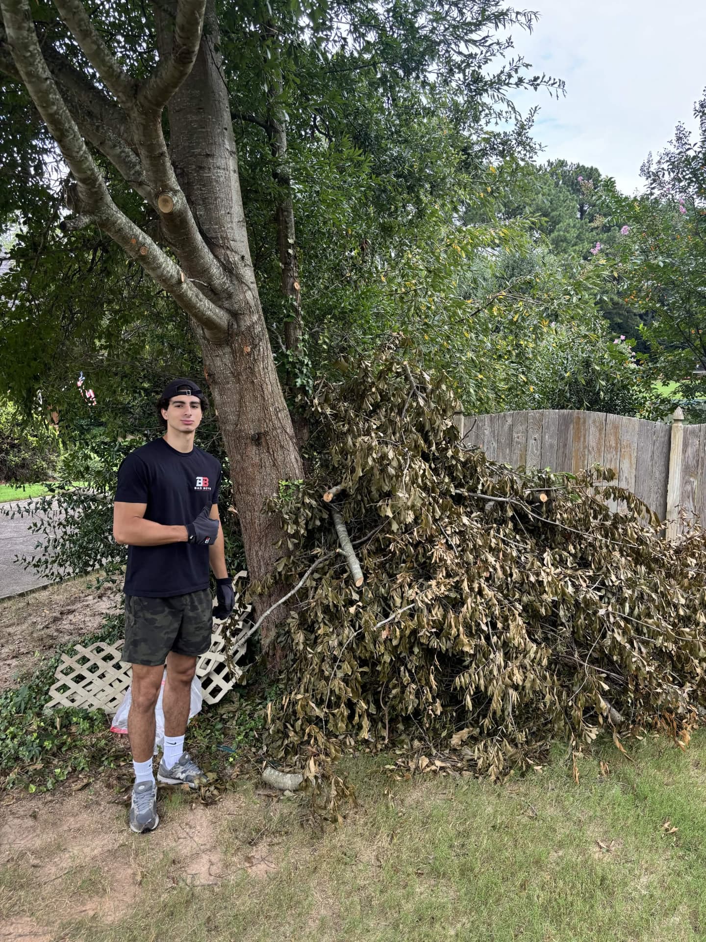 Bad Boys Junk Removal crew member in front of a large yard debris and brush pile